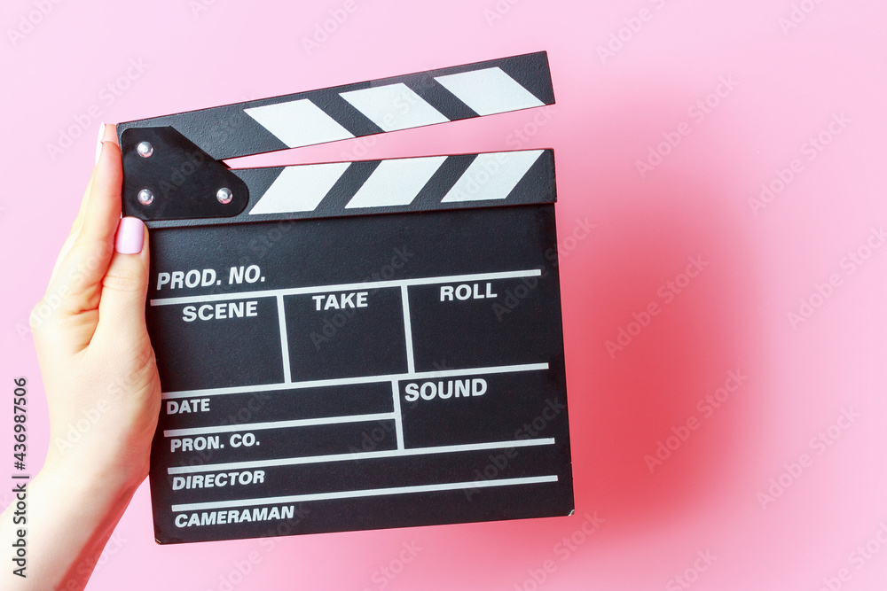 female hand holding a movie clapper board close-up on pink background.