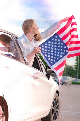 Canvas Print Young millennial blonde woman looking from car with american flag