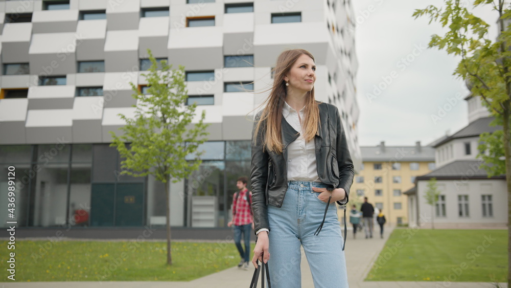 Stylishly dressed girl having fun outdoors in jeans clothes and leather jacket. Looks happy and pleasant. Look chic. Portrait of a female student on the background of the building. With nice Makeup Stylishly dressed girl having fun outdoors in jeans clothes and leather jacket. Looks happy and pleasant. Look chic. Portrait of a female student on the background of the building. With nice Makeup