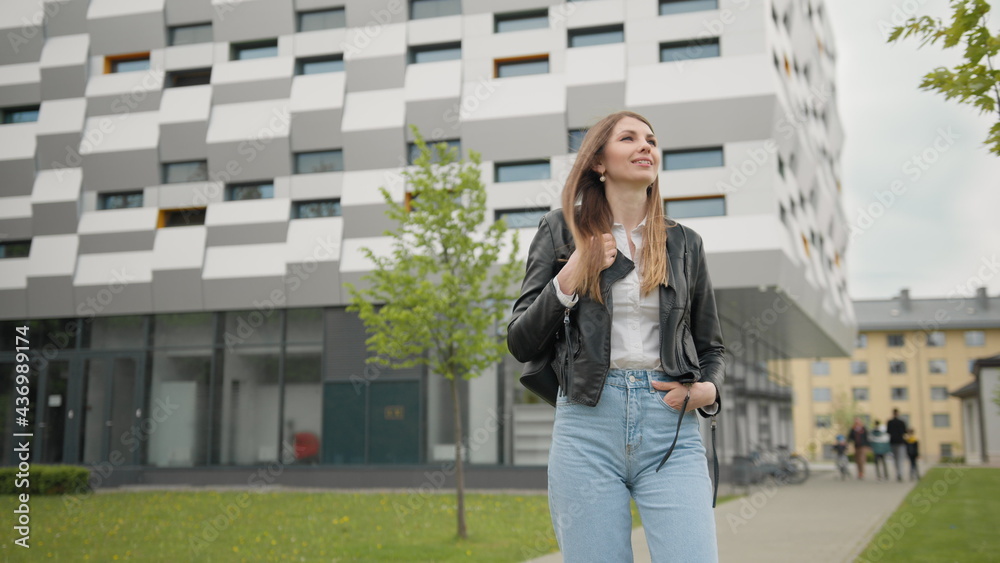 Fototapeta premium Stylishly dressed girl having fun outdoors in jeans clothes and leather jacket. Looks happy and pleasant. Look chic. Portrait of a female student on the background of the building. With nice Makeup