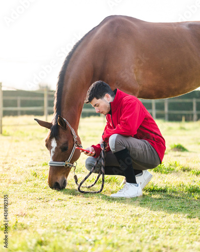 Young man browsing smartphone near horse grazing in ranch