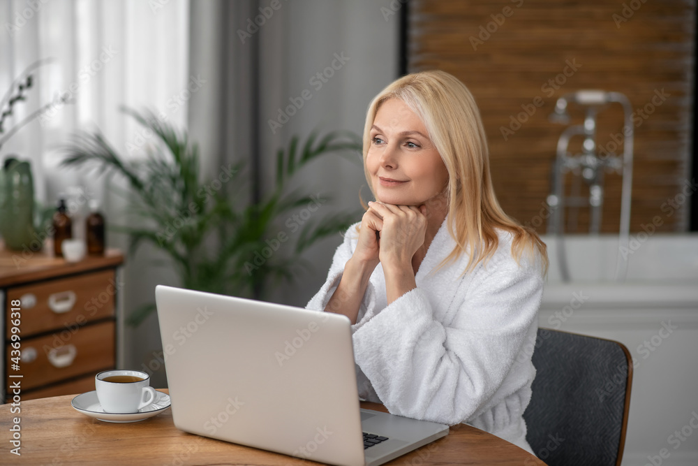 Pretty blonde woman sitting at the laptop and looking thoughtful Pretty blonde woman sitting at the laptop and looking thoughtful