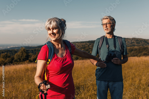 Active senior couple hiking in nature with backpacks, enjoying their adventure at sunset.