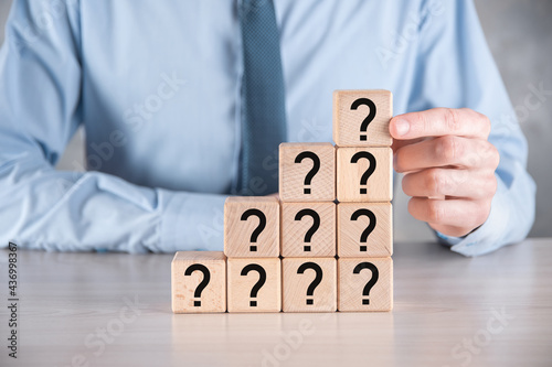 Businessman hold and put wooden cube block shape with question marks on grey table. Space for text.concept for confusion, question or solution