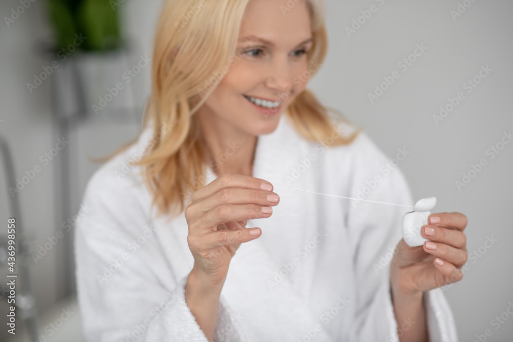 A good-looking smiling woman cleaning her teeth with a dental floss A good-looking smiling woman cleaning her teeth with a dental floss