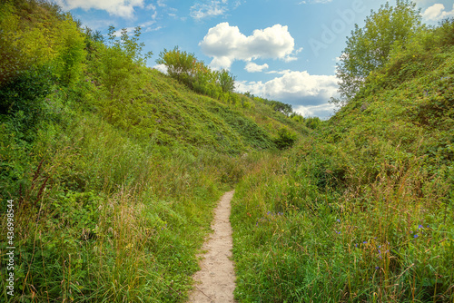 Summer landscape, road to clouds, path between hills overgrown with fresh grass and white clouds and blue sky in front