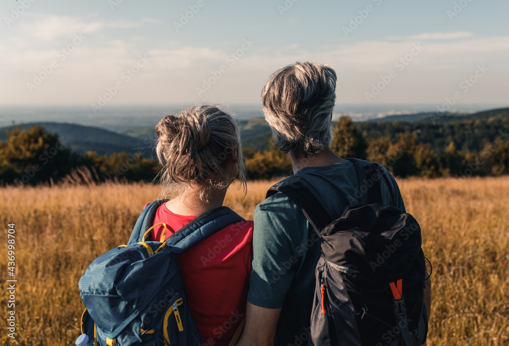 Active senior couple hiking in nature with backpacks, enjoying their adventure at sunset.