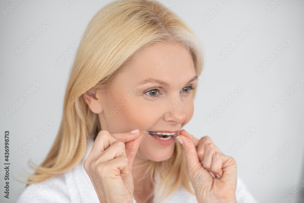 A portrait picture of a woman brushing her teeth with a dental floss