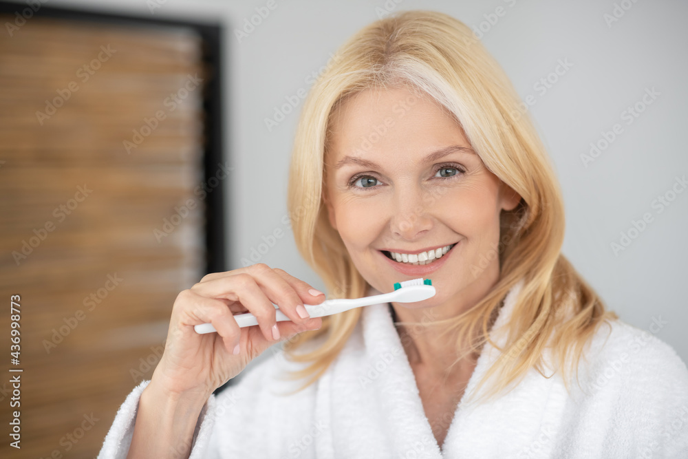 Smiling blonde woman brushing her teeth and looking happy Smiling blonde woman brushing her teeth and looking happy