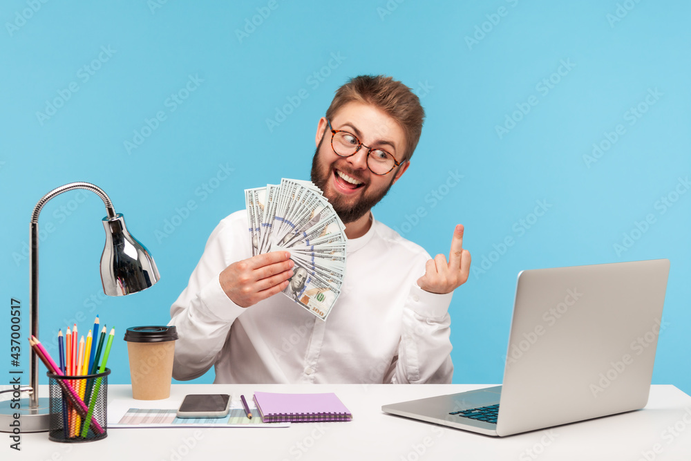 Happy funny man with beard showing fuck gesture with middle finger and dollar cash to camera on laptop talking video call, bragging with job promotion. Indoor studio shot isolated on blue background Happy funny man with beard showing fuck gesture with middle finger and dollar cash to camera on laptop talking video call, bragging with job promotion. Indoor studio shot isolated on blue background