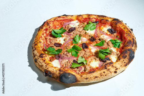 Delicious Italian wood-fired pizza with tomato sauce, mozzarella, olives and tuna on a gray background. Hard light.
