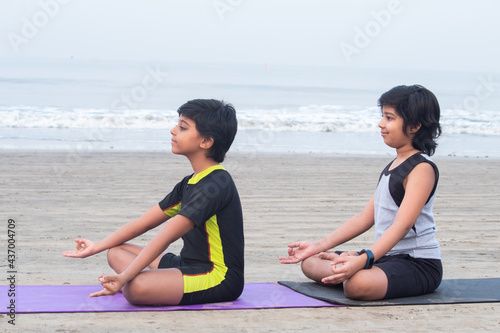 Profile of two boys sitting in lotus position practicing yoga on exercise mat at beach