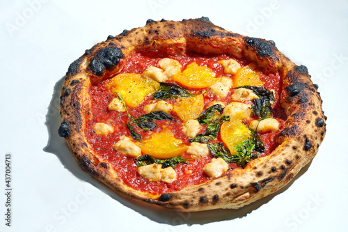 Delicious italian wood fired pizza with tomato sauce, yellow tomatoes and vegan cheese on a gray background. Hard light.