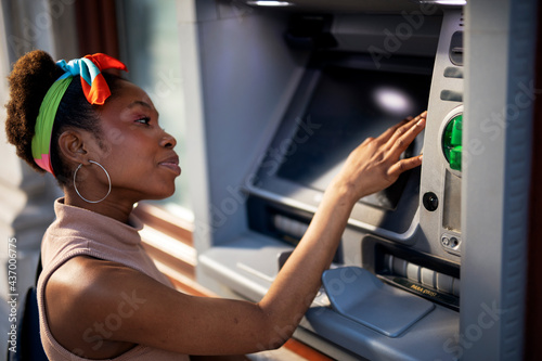 Beautiful african womn using ATM machine. Attractive young woman withdrawing money from credit card at ATM.