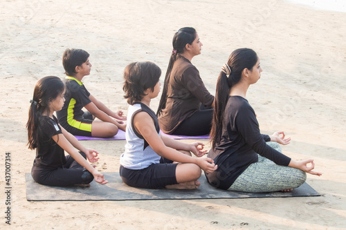 Two women with children practicing yoga in lotus position at beach