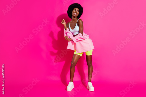 Photo of adorable funky dark skin woman dressed crop top smiling dancing looking empty space isolated pink color background © deagreez