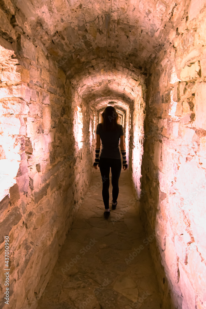 Silhouette of woman walking in corridor of ancient fortress made of stones