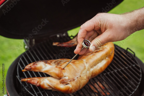 Men chef measuring rabbit meat temperature. Gourmet barbecue- smoking, baking, roasting process. Ceramic BBQ grill in homes terrace.