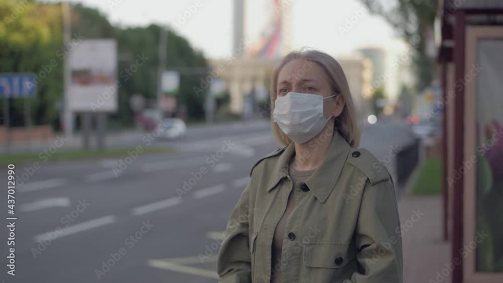 A woman stands at a bus stop in the city center and removes a medical mask from her face. A woman stands at a bus stop in the city center and removes a medical mask from her face.