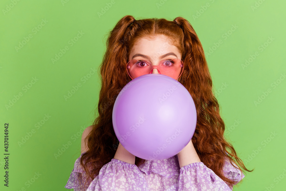 Photo of ginger hairstyle young lady blow balloon wear violet blouse spectacles isolated on green color background Photo of ginger hairstyle young lady blow balloon wear violet blouse spectacles isolated on green color background