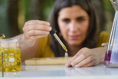 Woman making essential oil sample with plant extracts and dropper, selective approach