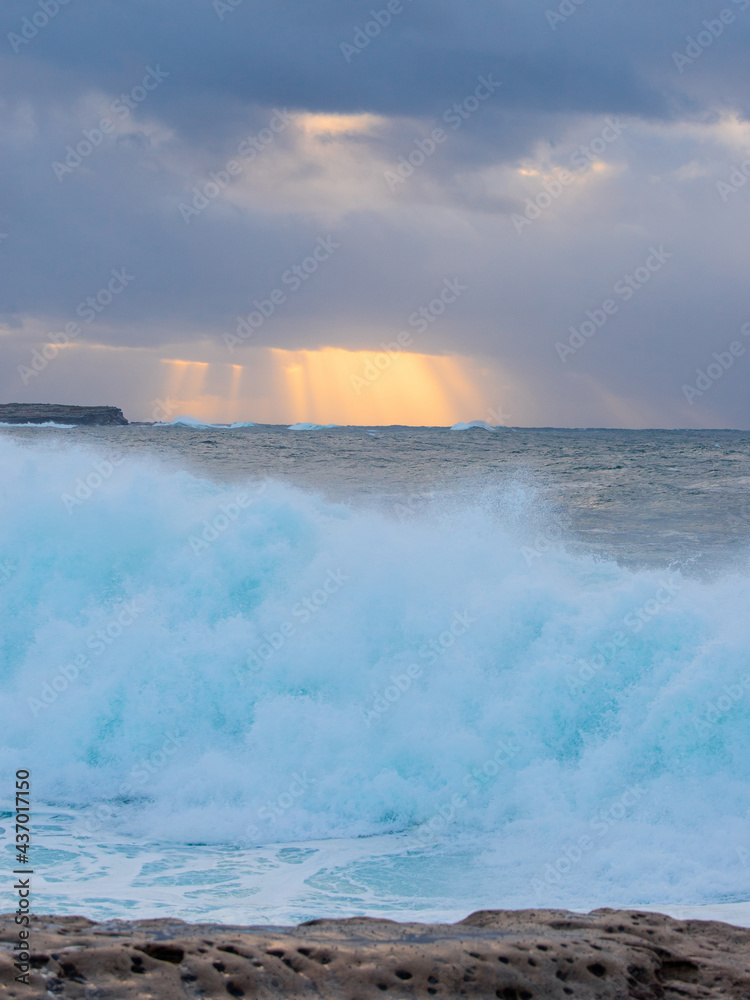 Fototapeta premium Ray of light over the wave breaking on the coast.
