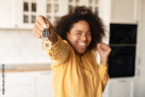 Joyful African-American woman holds keys with trinket in shape of little cute house, selective focus on the keys photo