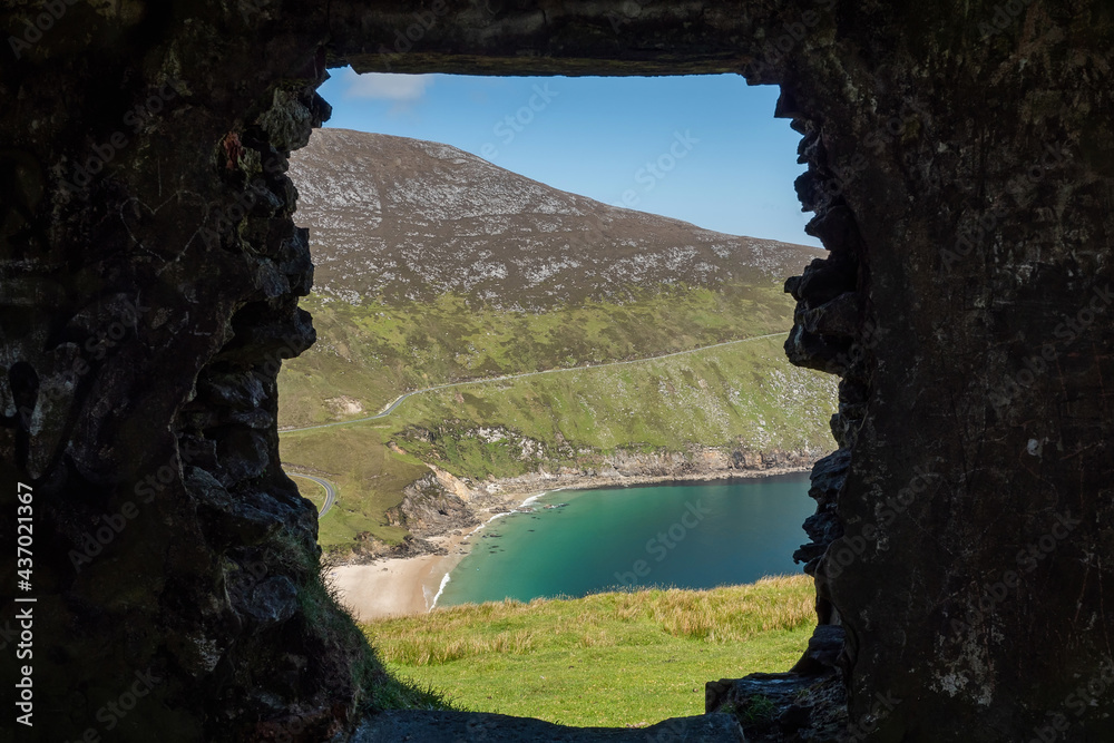 View on Keem beach from a window of an old building. Achill island, county Mayo, Ireland. Beautiful sandy beach with clear blue water. Bright nature landscape framed by dark building