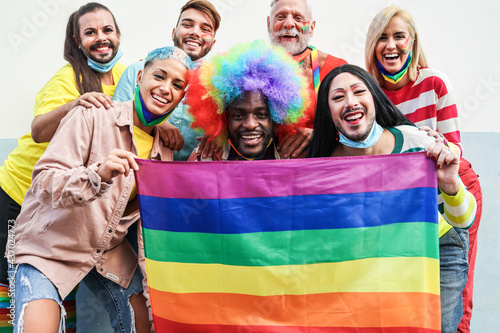 Gay people smiling at pride parade with LGBT flags while wearing protective face mask - Main focus on left girl face