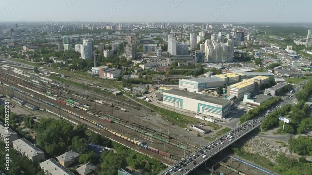 Aerial view of Rail Station with freight trains and bridge with road junction in a big city. High residential buildings nearby, industrial zone and office buildings. There are many trees in the city. Aerial view of Rail Station with freight trains and bridge with road junction in a big city. High residential buildings nearby, industrial zone and office buildings. There are many trees in the city.
