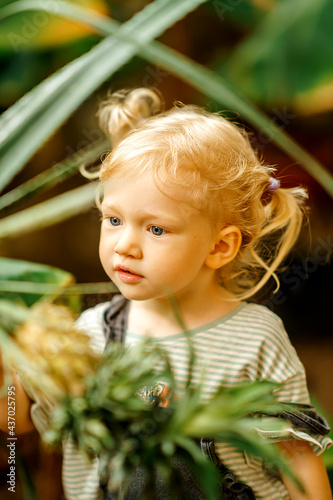 close up Portrait of a cute adorable blonde Caucasian girl watching the plants grow in the greenhouse. The child is studying nature. Early development concept.