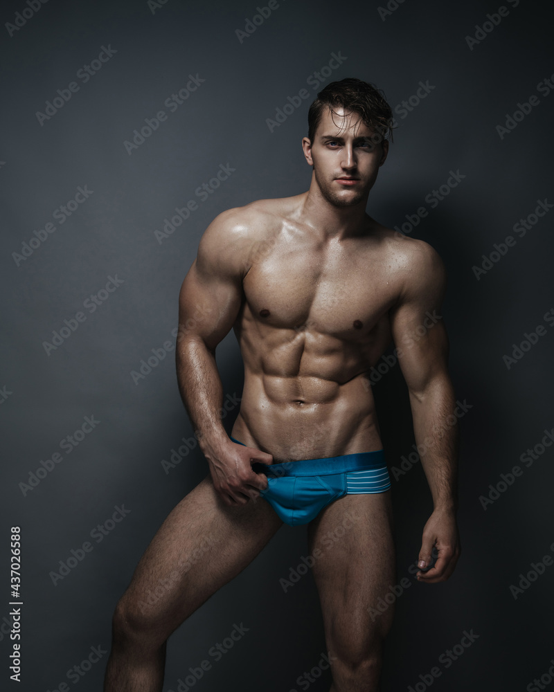 Shirtless man in blue underwear at grey background in studio Shirtless man in blue underwear at grey background in studio