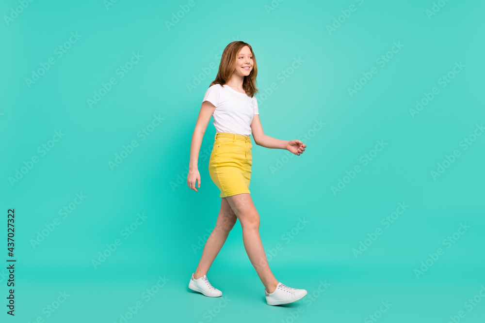 Full length body size photo smiling schoolgirl walking forward looking copyspace isolated vivid teal color background Full length body size photo smiling schoolgirl walking forward looking copyspace isolated vivid teal color background