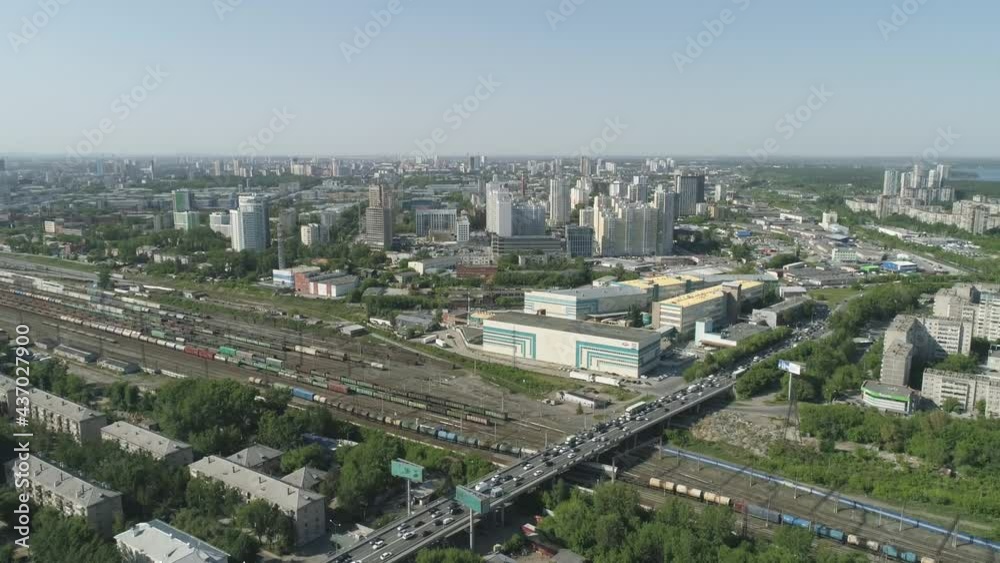 Aerial view of Rail Station with freight trains and bridge with road junction in a big city. High and low residential buildings nearby, industrial zone and office buildings. There are many trees in th Aerial view of Rail Station with freight trains and bridge with road junction in a big city. High and low residential buildings nearby, industrial zone and office buildings. There are many trees in th