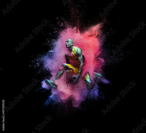 One young sportsman basketball player in explosion of colored neon powder isolated on black background © master1305