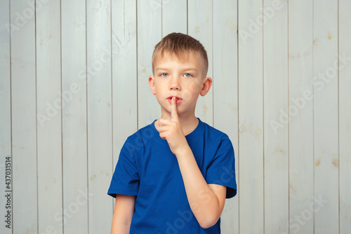 Portrait of cute preteen boy keeping finger at her mouth, saying Shh, Hush, Tsss. Silence and secret concept photo