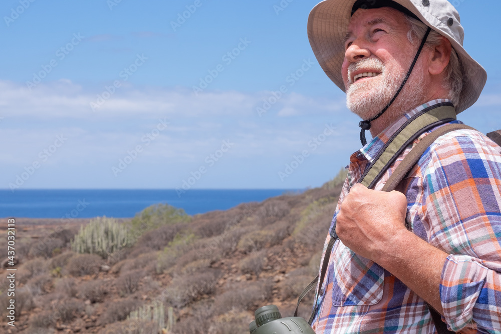 Naklejka premium Senior man traveler enjoying outdoors excursion walking between mountain and sea, wearing cap and backpack