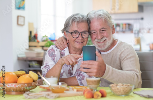 Smiling senior couple looking cellphone during breakfast at home
