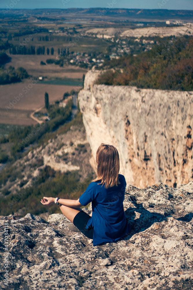 Young woman sits on a rock, looking at the landscape and enjoying the view and fresh air.