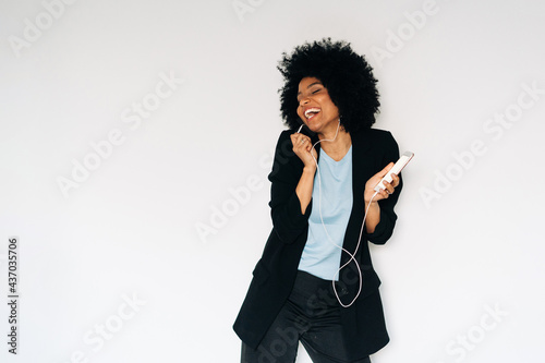 Happy black woman dancing and singing while listening to music on smartphone