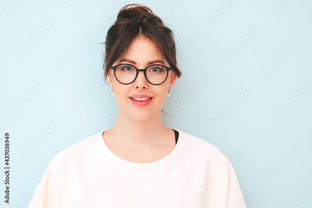 Young beautiful smiling female in trendy summer hipster clothes. Sexy carefree woman posing near light blue wall in studio. Positive model having fun indoors. Cheerful and happy in eyewear