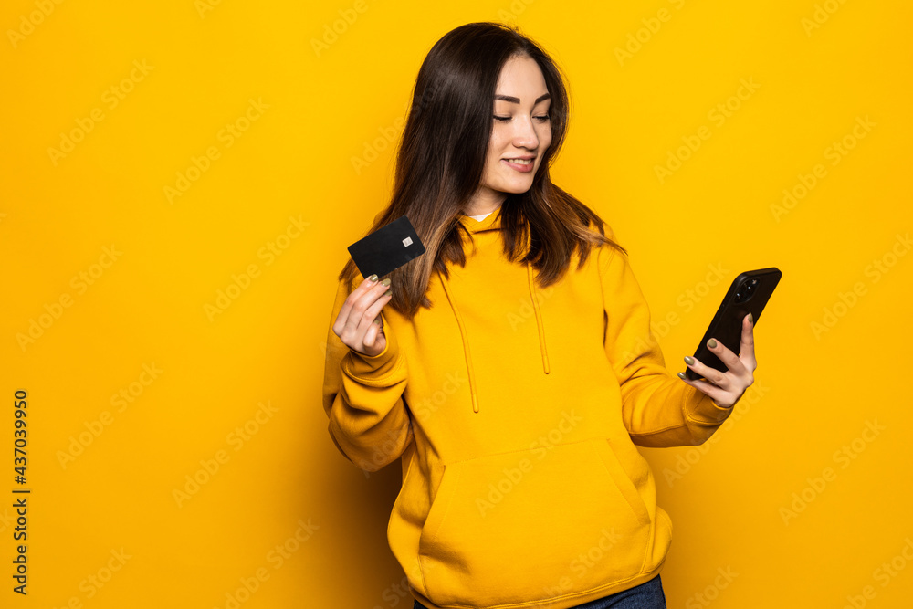 Young Asian woman using credit card and smart phone for online shopping, payment over yellow background Young Asian woman using credit card and smart phone for online shopping, payment over yellow background