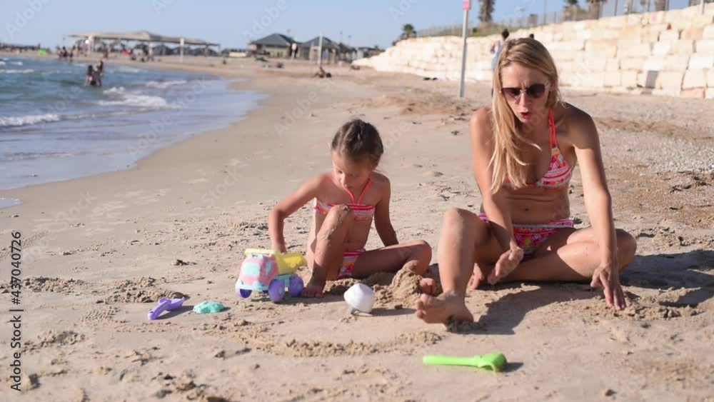 Mom and daughter in summer on beach by sea in same swimwear. Pretty young woman with child sculpt from sand. vacation and travel on sea on holiday. Mom and daughter in summer on beach by sea in same swimwear. Pretty young woman with child sculpt from sand. vacation and travel on sea on holiday.