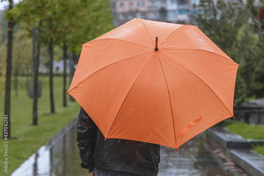 A man walks down the street during heavy rain with an orange umbrella