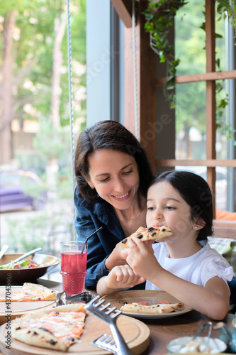Mom and daughter eat pizza in a cafe, restaurant.