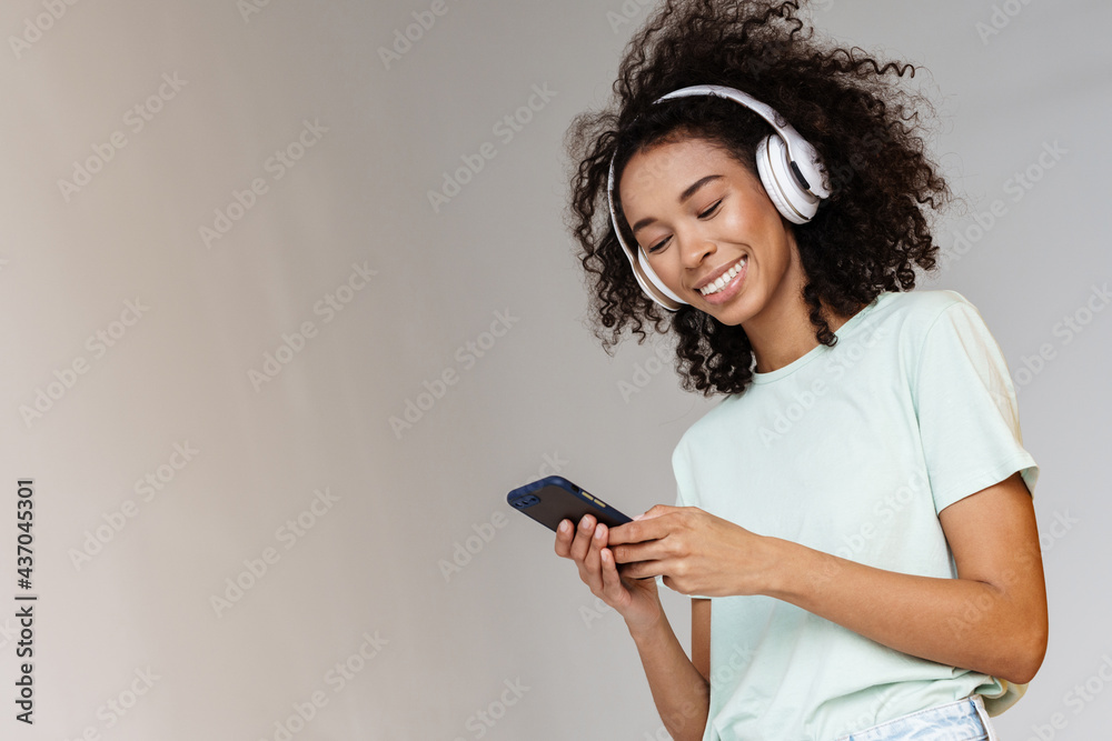 Young african woman in headphones smiling while using mobile phone Young african woman in headphones smiling while using mobile phone