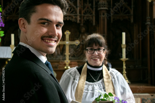 Gay groom waits for his husband at altar in church with vicar in the background photo