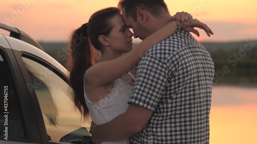 A man and a woman are hugging on the shore of the beach while standing at sunset by the car, a married couple traveling by personal transport, meeting the dawn together, relationship in a couple of