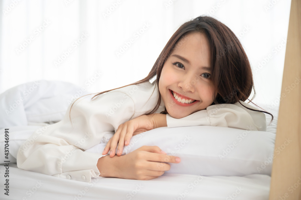 Young asian woman waking up in the morning on bed. She showing face out the blanket and smile feeling happy Young asian woman waking up in the morning on bed. She showing face out the blanket and smile feeling happy