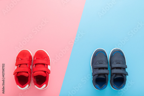 Red and dark blue sport shoes for little boy and girl on light blue pink table background. Pastel color. Children footwear. Empty place for text. Top down view.